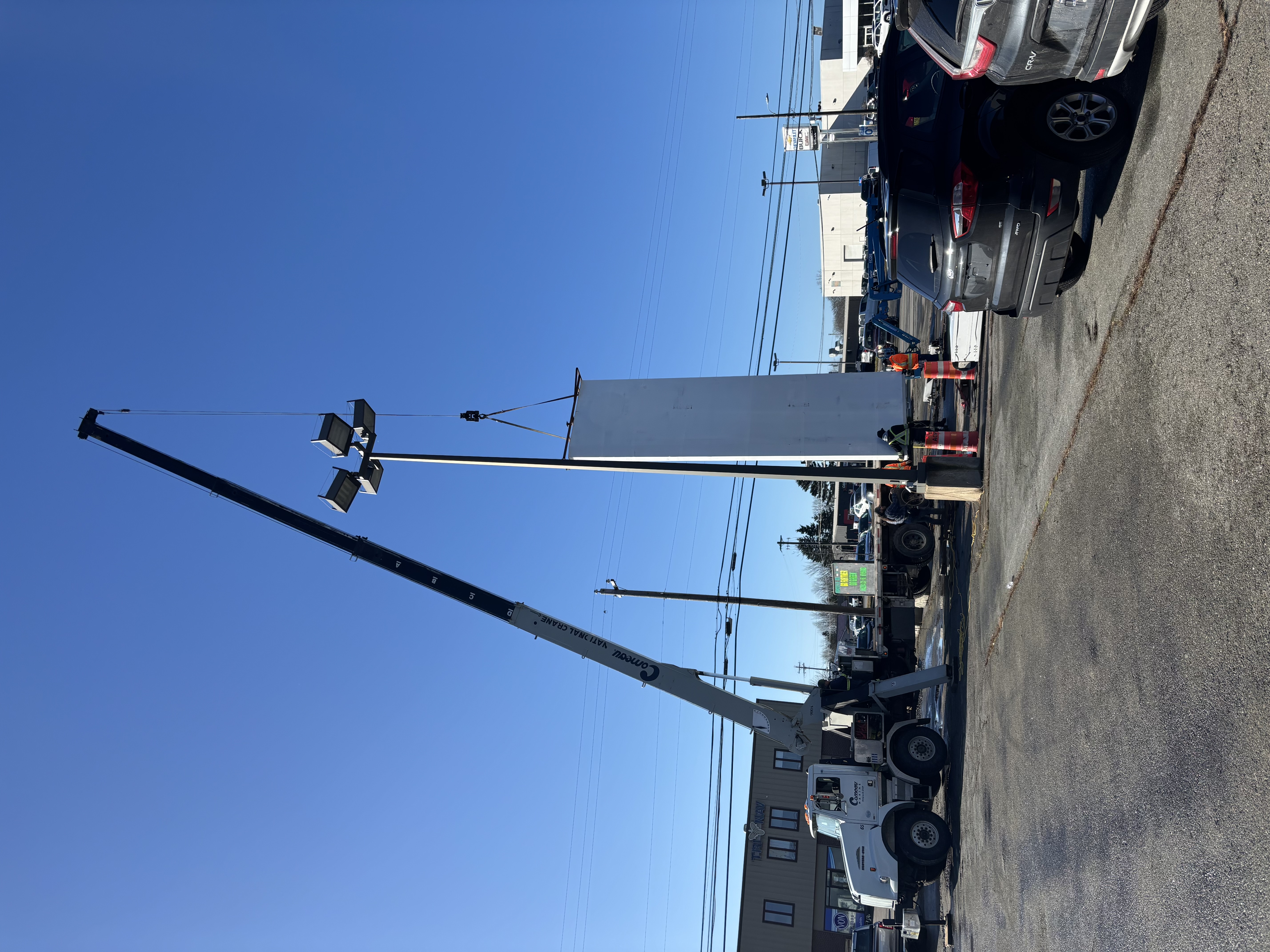 Crew guiding a crane-lifted Mazda pylon sign into position during a commercial installation